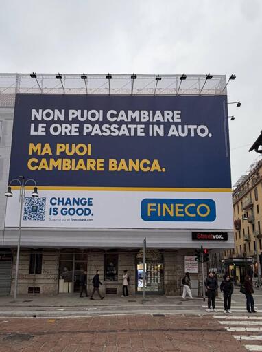 Foto del cartello pubblicitario FINECO che occupa quasi tutta la facciata di un edificio di 3 piani. Il testo del cartellone è nel post. Sotto si vede il piano terra e alcune persone che ci camminano davanti